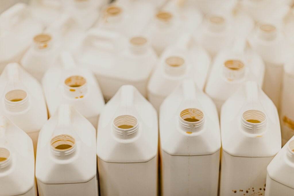 Several white, square plastic jugs with open caps are closely packed together. The jugs appear to be empty, some stained or having remnants of working chemicals inside. The photo is taken from above, showcasing the uniform arrangement of the jugs.