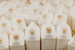 Several white, square plastic jugs with open caps are closely packed together. The jugs appear to be empty, some stained or having remnants of working chemicals inside. The photo is taken from above, showcasing the uniform arrangement of the jugs.