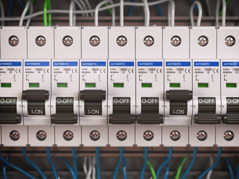 Close-up of several electrical circuit breakers lined up in a row inside an electrical panel. Each breaker, showcasing "I-ON" and "O-OFF" labeled switches, is accompanied by tangled colored wires running behind them, ensuring smart safety and efficient control.