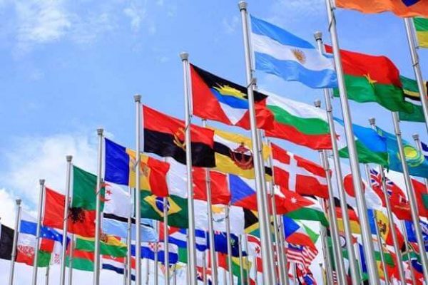 Image showing multiple national flags from various countries displayed on flagpoles, waving against a bright blue sky. The flags exhibit a diverse range of colors and designs, symbolizing international representation and unity, with all installations done with meticulous OSHA compliance.