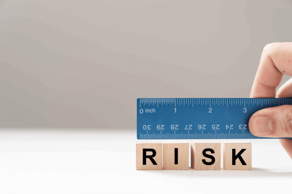 A hand holding a blue ruler measures wooden blocks that spell "RISK," representing the importance of precise planning in Emergency Action Plans (EAP).