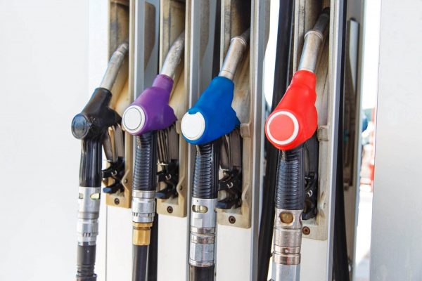 Four fuel pump nozzles are attached to a gas station pump. They are colored black, purple, blue, and red, respectively. The nozzles are hanging in their holders, ready for use, ensuring you can refuel safely and efficiently.